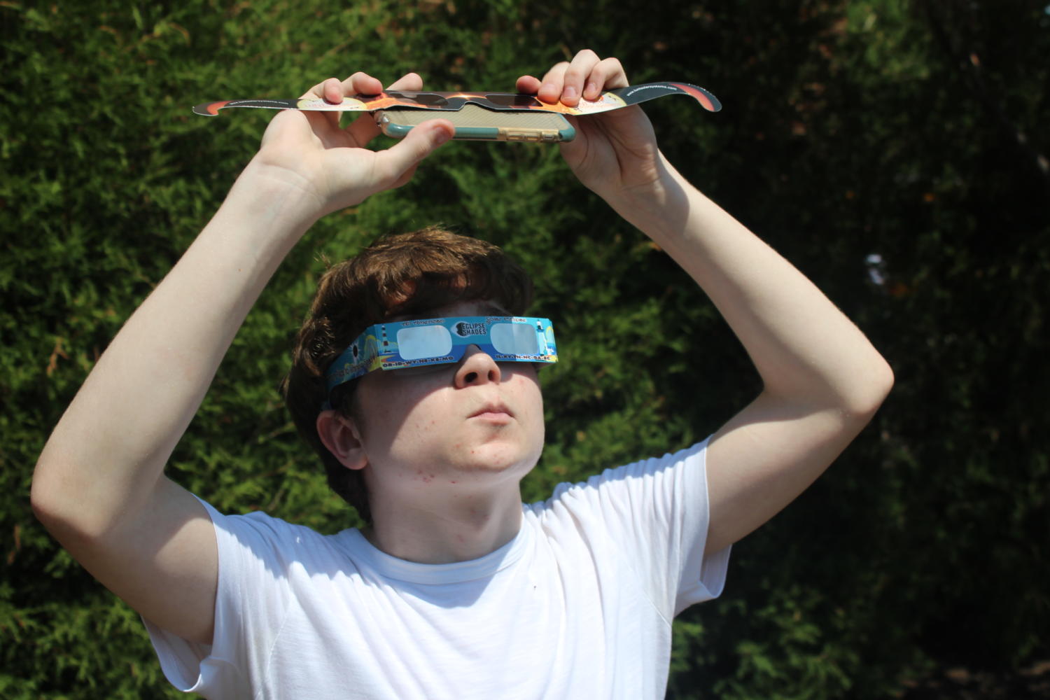 Sophomore Aden Adams uses eclipse glasses to protect his phone while taking a picture of the eclipse.