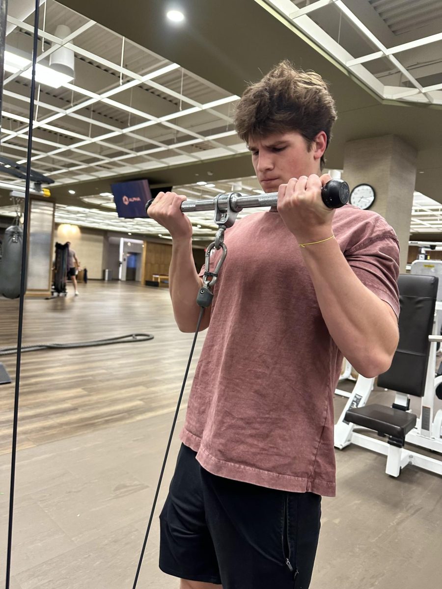 Carter Hanley (12) bicep curls a resistance bar at Lifetime Fitness Nov. 19. He started lifting at the beginning of high school and has continued since. “I know I can keep going and keep on progressing,” Hanley said. “I love seeing the results of the work. it’s really satisfying and pays off.”